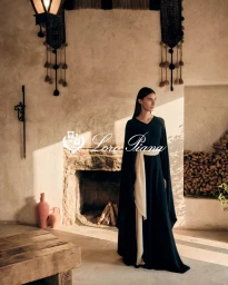 Amira Al Zuhair wearing a dark gown with a cream sash standing inside a rustic room with a fireplace for Loro Piana