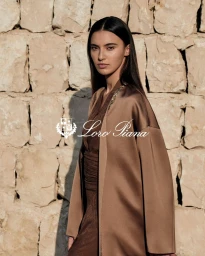 Model Amira Al Zuhair in a brown silk coat against a textured stone wall for Loro Piana Ramadan campaign