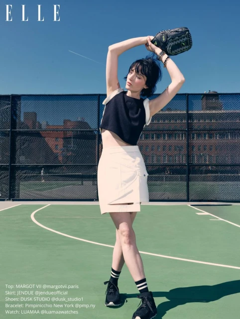 Model holding a baseball mitt on a tennis court wearing a black crop top and white mini skirt for Elle Slovenia