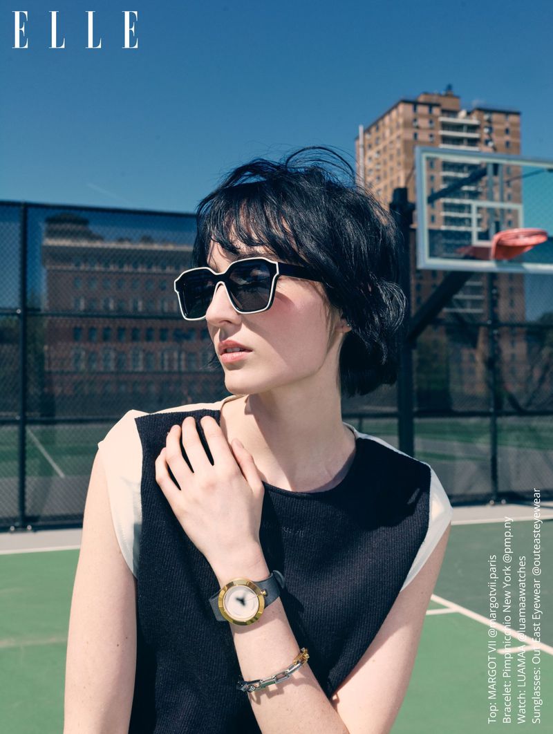 A dark-haired woman wearing oversized sunglasses and a black and white top on an outdoor tennis court.