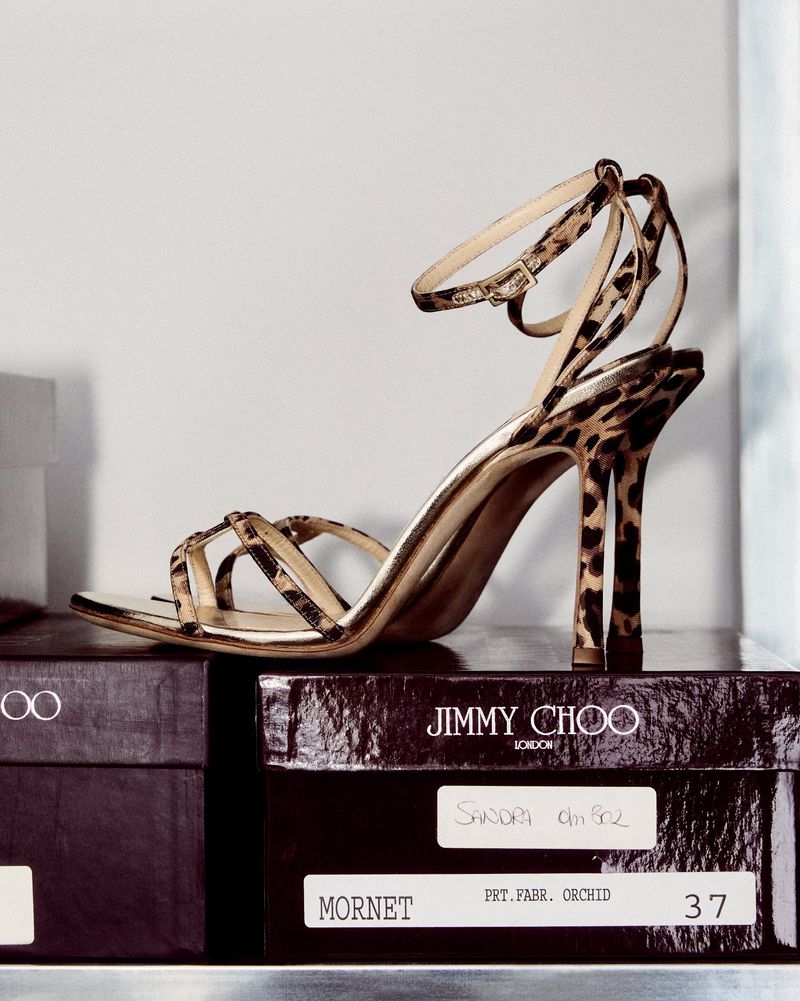 Leopard print Jimmy Choo stiletto sandal on shoe boxes. The footwear features thin ankle straps and is placed indoors.
