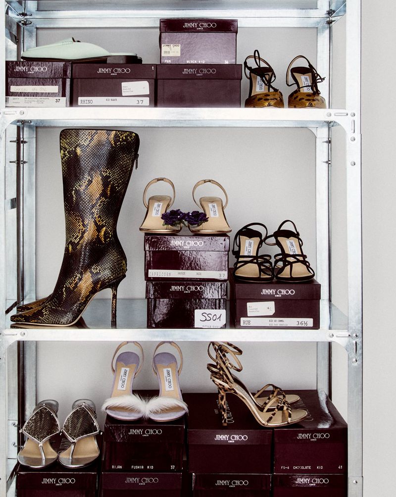 Display of Jimmy Choo shoes on a metal shelving unit. Shoe boxes with brand logos are stacked behind the footwear.