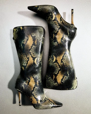 Two snake-print knee-high heeled boots are displayed on a neutral surface, one upright and one angled.