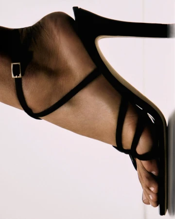 Close-up of a woman's foot in a black strappy high-heel sandal against a plain white background. High fashion shoe detail shot.