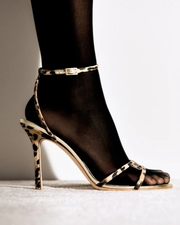 Close-up studio shot of a woman's foot wearing black tights and a high-heeled sandal with an animal print strap.
