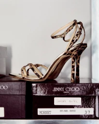Leopard print strappy high heel sandal resting on top of branded dark boxes against a white background.