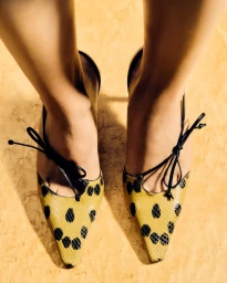 Close-up overhead shot of feet wearing yellow and black patterned pointed-toe shoes with thin black bows.