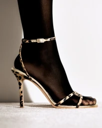 Close-up of a leopard print high heel sandal worn with black sheer tights against a clean white seamless studio background.