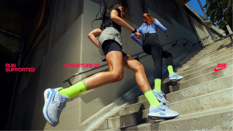 Two women in sportswear run up concrete stairs. Athletic footwear, neon socks, urban concrete environment, natural light, activewear.