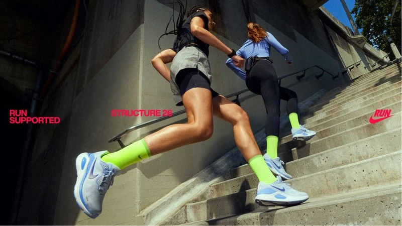 Two women in sportswear run up concrete stairs. Athletic footwear, neon socks, urban concrete environment, natural light, activewear.