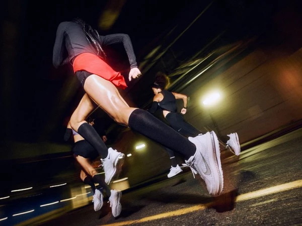 Dynamic action shot of a group of runners in athletic wear, showcasing motion blur in a dark, urban environment, possibly a tunnel.