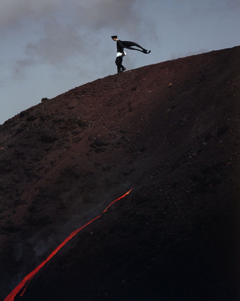 Adult male in dark suit walks down volcanic slope with lava stream. Dramatic landscape and unusual fashion-forward editorial concept.