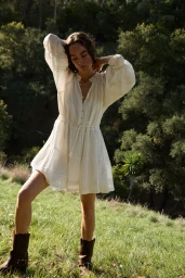 Model wearing a white dress and brown boots standing on a grassy hill outdoors