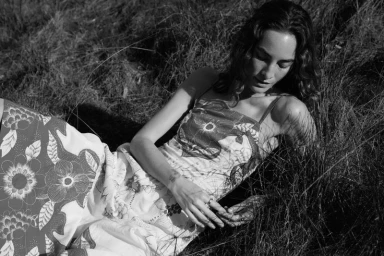 Model Heather Kemesky in a floral dress lying in tall grass in a black and white portrait captured by Sylve Colless.