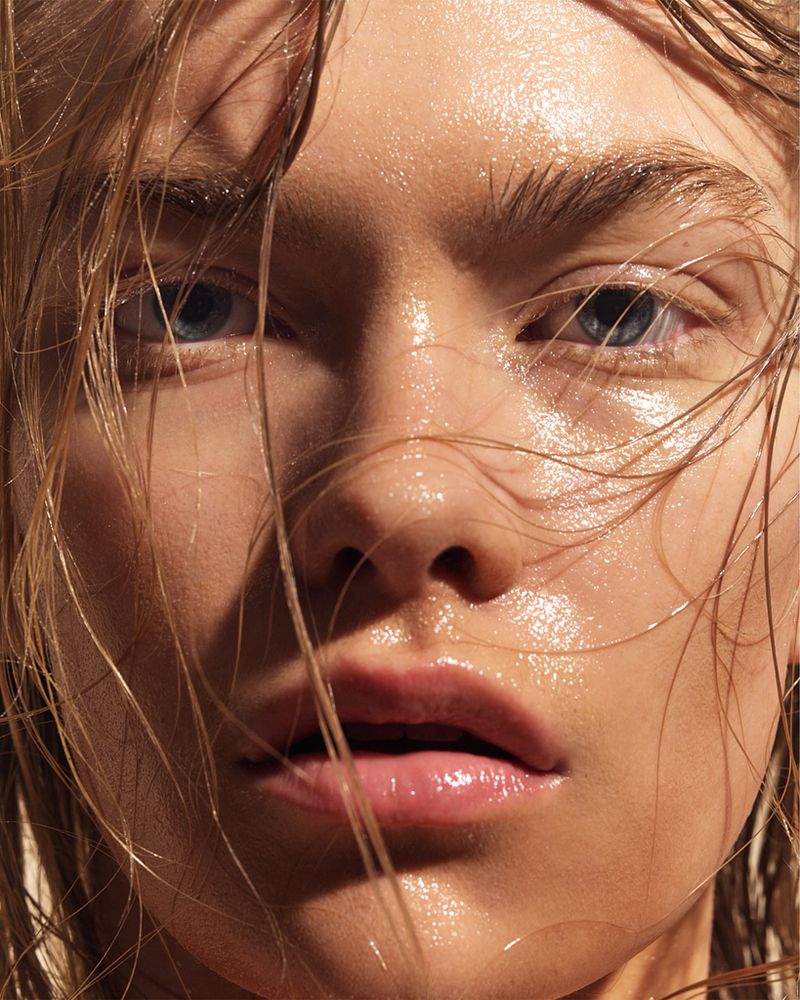 Close-up portrait of a young woman with wet blonde hair and glistening skin, gazing directly at the camera with a serious expression.