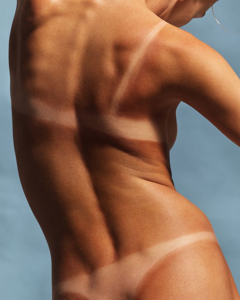 Back view of a person with defined back muscles and a significant tan line, set against a simple, light blue backdrop.