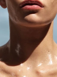Extreme close up of a model chin, lips and neck with dewy glowing summer skin under bright sunlight