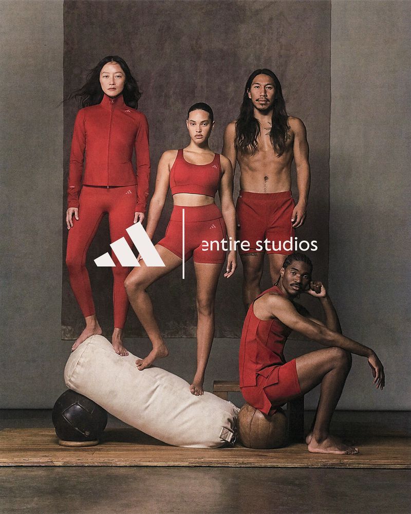 Group of four athletic adults in matching red activewear posing in a studio; Adidas logo is in view alongside gym props.