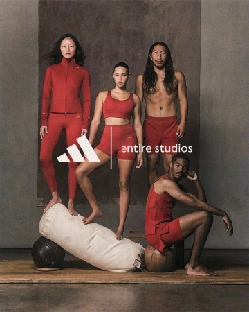 Group of four athletic adults in matching red activewear posing in a studio; Adidas logo is in view alongside gym props.