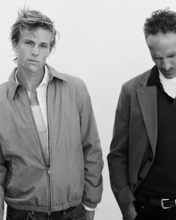 Monochrome portrait of two male models wearing casual jackets against a plain white studio backdrop.