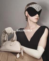Model in black top wearing crystal visor and white gloves holding a light handbag for Balenciaga
