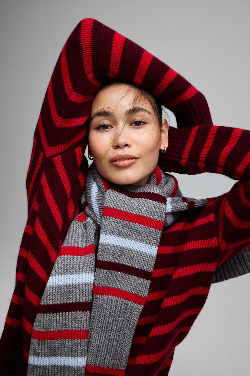 Portrait of a woman in a striped sweater and scarf, posing with hands up. Red and burgundy colors, studio lighting, neutral background.