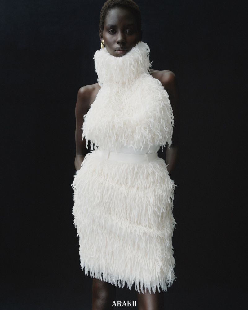 Fashion model in a white, feathered halter dress posing against a dark backdrop. Elegant studio portrait.
