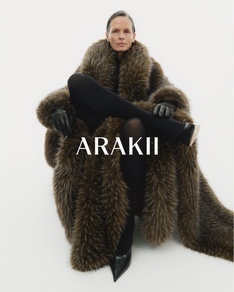 A person wearing an oversized fur coat and black leather gloves sitting against a white background for a fashion advertising campaign.