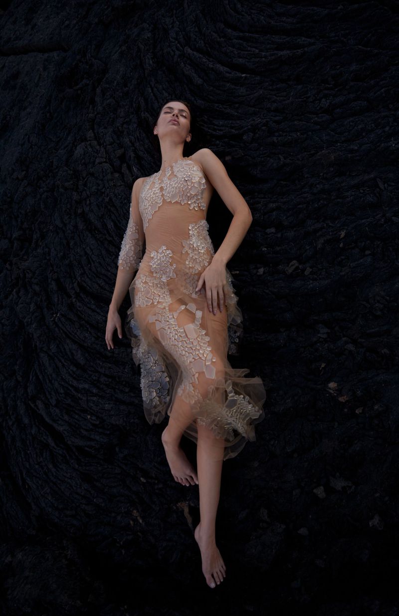 Adult female poses in beige, floral-patterned gown on swirling black background, shot from eye-level.