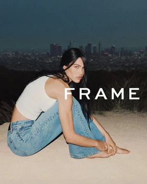Amelia Gray sitting outdoors at dusk wearing a white crop top and blue denim jeans against a city skyline