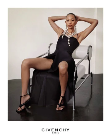 Model wearing black dress and layered pearl necklace seated in a modern chair for Givenchy Summer 2026