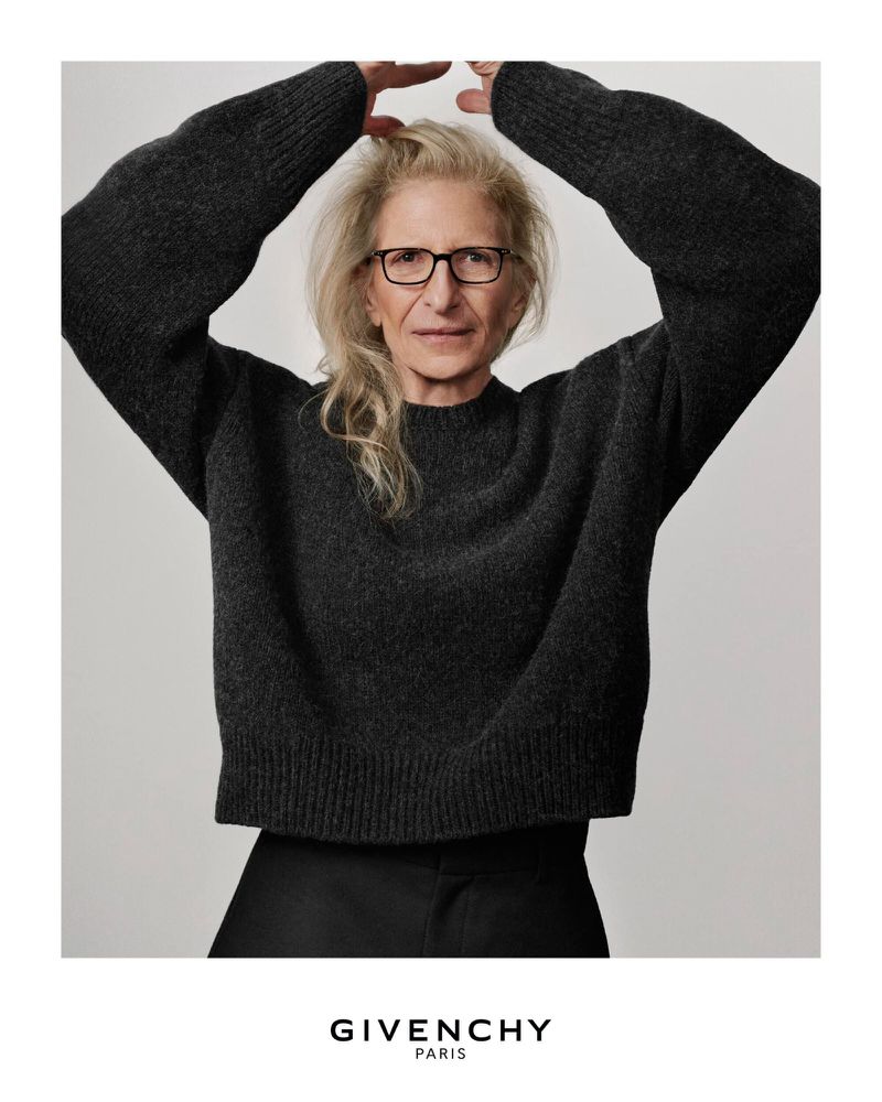 Fashion portrait of an elderly woman with glasses, wearing a grey sweater, posing in a bright photo studio for a Givenchy advertisement.