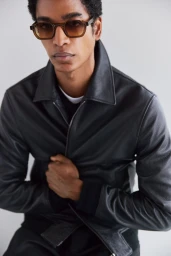 Man wearing a black leather jacket and tinted sunglasses against a seamless grey studio background
