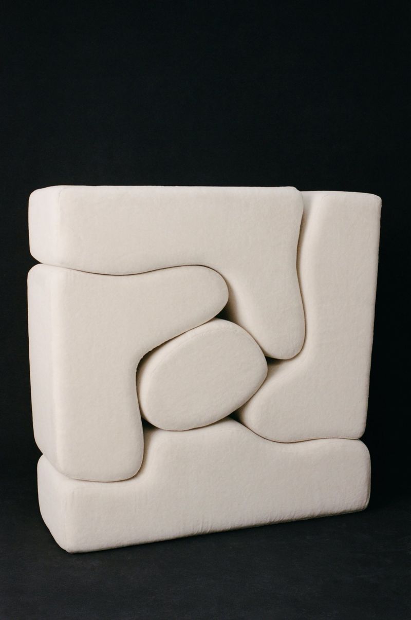Abstract geometric sculpture in off-white with interlocking shapes against a dark background, creating a modern and minimalist aesthetic.