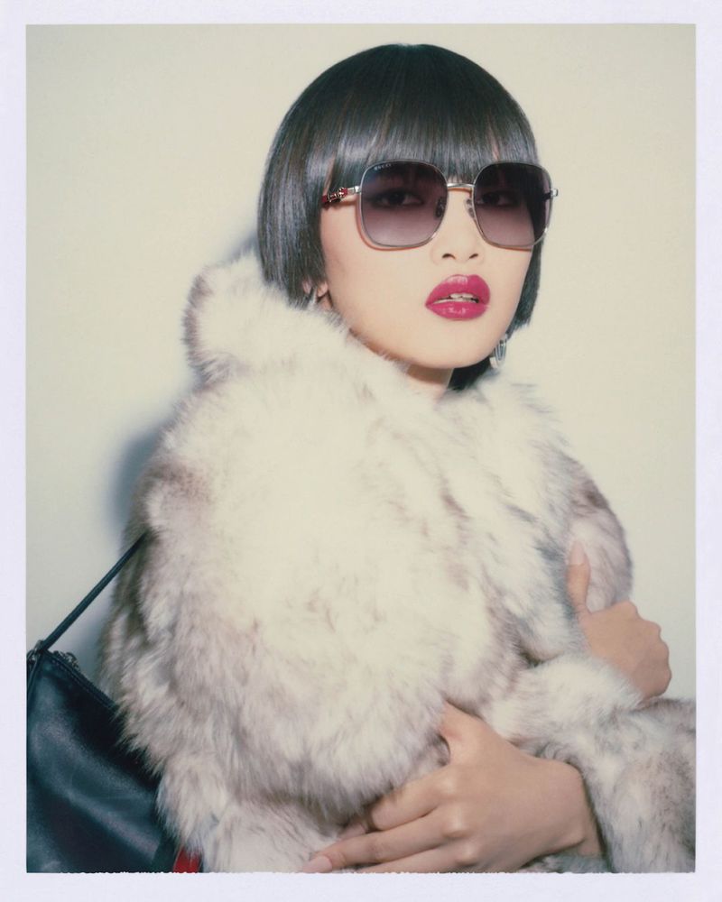 Stylish woman in fur coat and sunglasses poses against a white backdrop, creating a fashion-forward and eye-catching visual statement.