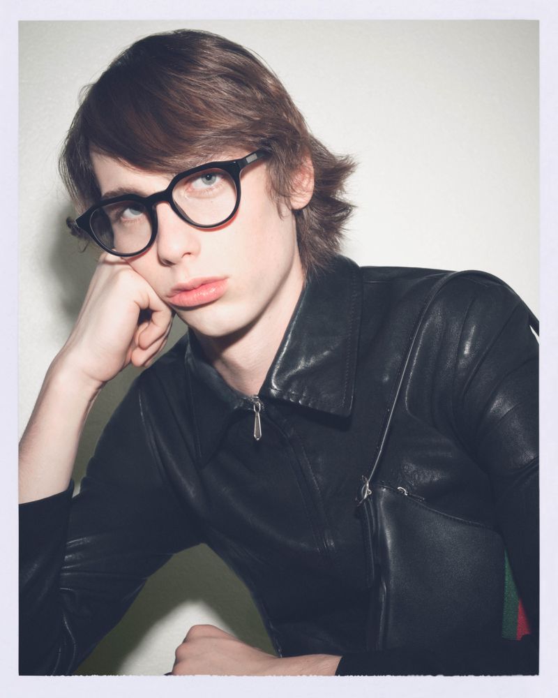 Portrait of a young adult male wearing glasses and a black leather jacket looking at the camera with a neutral expression.