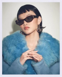 Model wearing tortoiseshell sunglasses and oversized blue faux fur coat against white wall