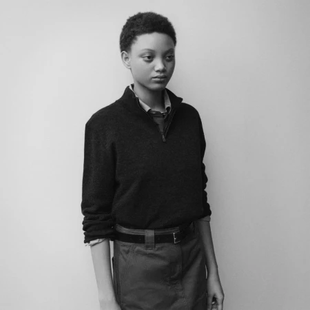 Model wearing dark quarter-zip sweater and belted skirt standing against plain studio background