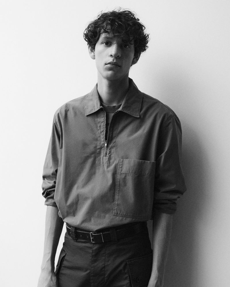 Black and white portrait of a young adult male in a casual shirt with dark curly hair against a neutral background, shot with studio lighting.