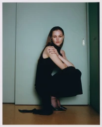 Model in black dress crouching against a pale green wall for Revolve campaign