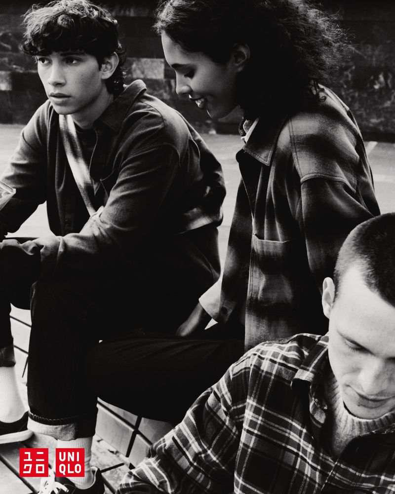 Three young adults sit together outdoors, wearing casual clothing. The shot is in black and white, with the Uniqlo logo visible.