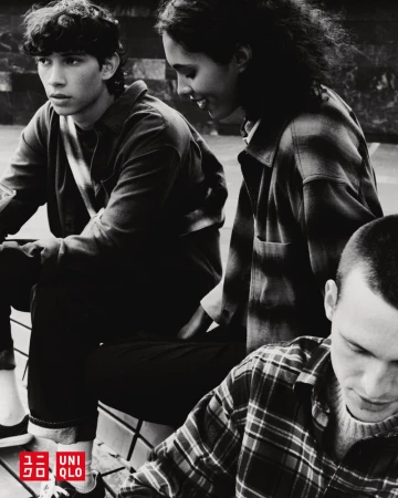 Three young adults sit together outdoors, wearing casual clothing. The shot is in black and white, with the Uniqlo logo visible.