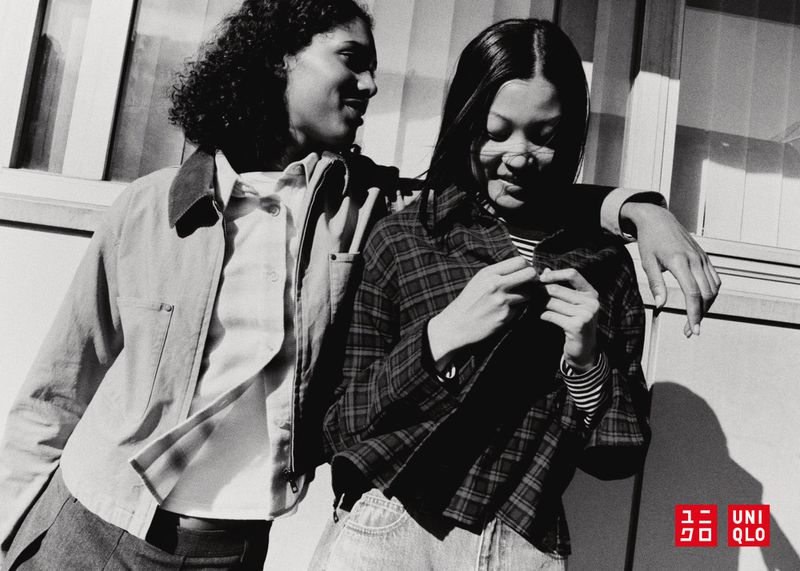 Two young women smile in a black and white fashion shot, wearing jackets, with the Uniqlo logo visible in the corner.