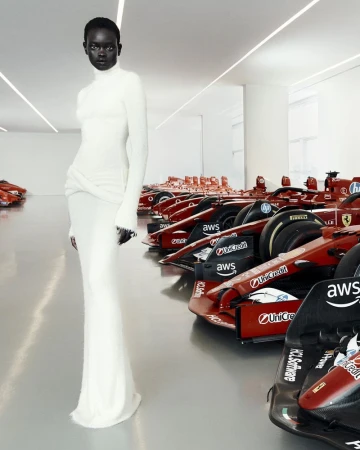 Elegant Black woman in a white dress poses in a showroom, surrounded by several red Formula One race cars, under bright white lighting.