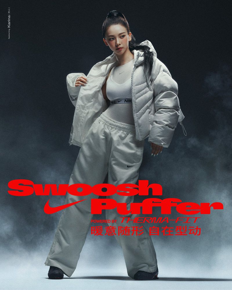 An adult woman poses in a Nike puffer jacket and sweatpants against a grey background with red Nike branding and some fog effects.