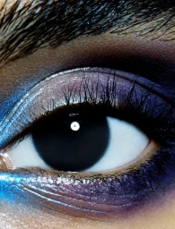 Extreme close-up of a human eye featuring dramatic blue and purple eyeshadow makeup and long dark eyelashes.