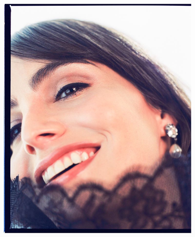 Close-up portrait of a smiling adult female with fair skin, brown hair, and an earring, partially veiled with black lace.