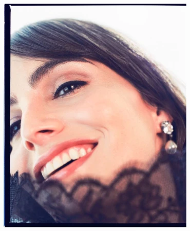 Close-up portrait of a smiling adult female with fair skin, brown hair, and an earring, partially veiled with black lace.