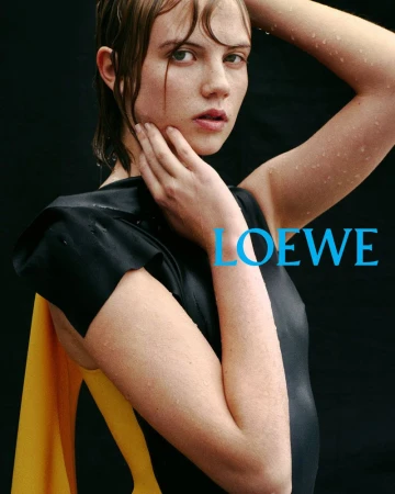 Headshot of a young adult woman with wet hair wearing a black top with yellow fabric against a black backdrop. Fashion photography.