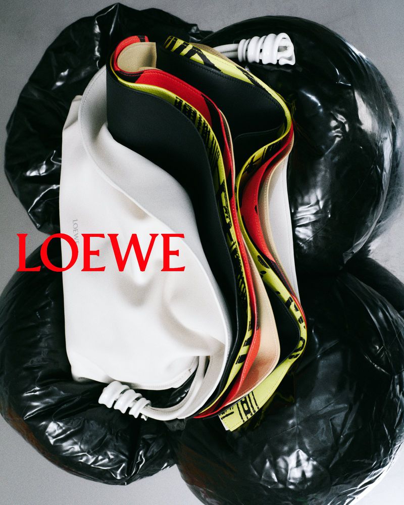 Fashion still life featuring a Loewe garment bag in white with black lining, artfully arranged on a stack of black plastic trash bags.